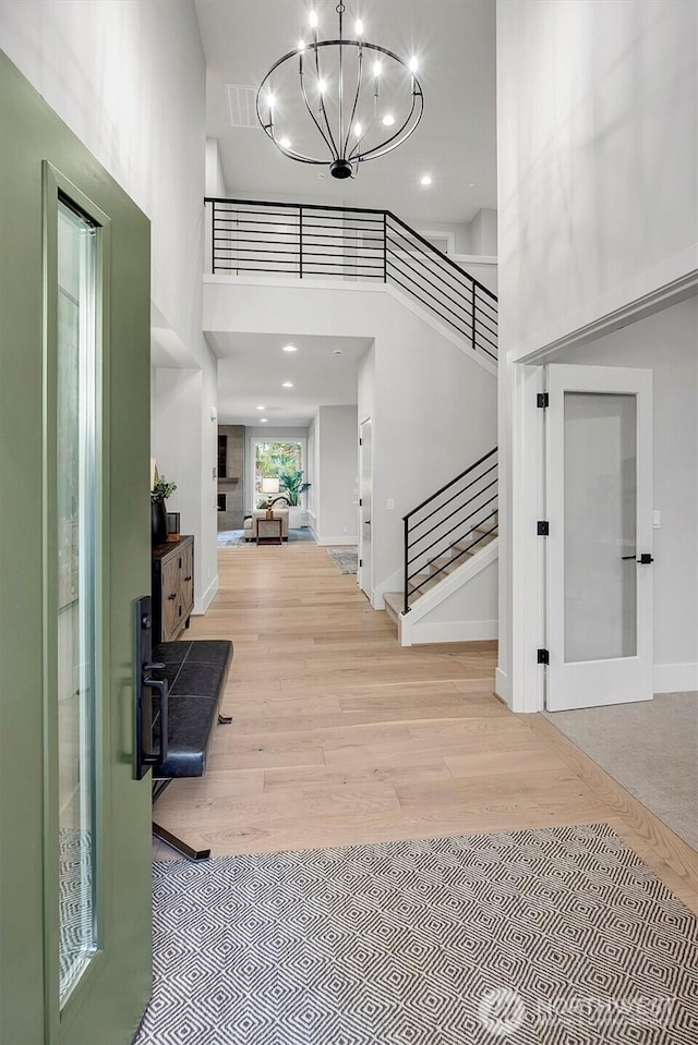 foyer entrance featuring stairway, wood finished floors, a towering ceiling, and a chandelier