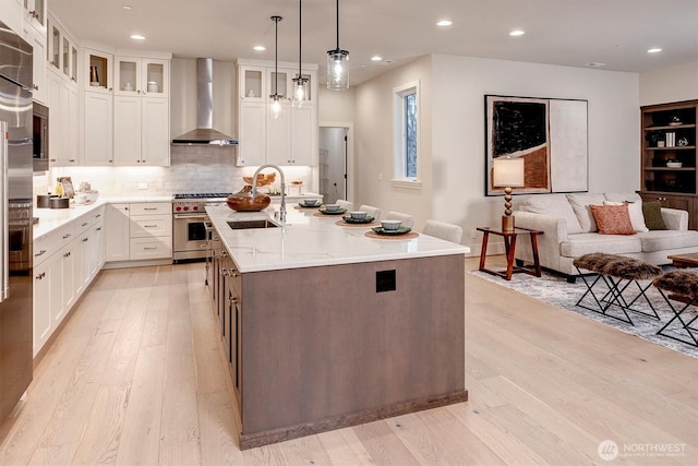 kitchen featuring a sink, light wood-type flooring, high end stainless steel range, and wall chimney range hood