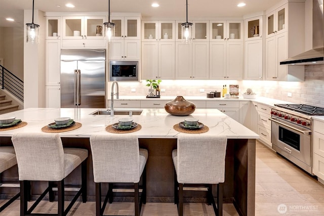 kitchen with built in appliances, white cabinets, wall chimney range hood, and a sink