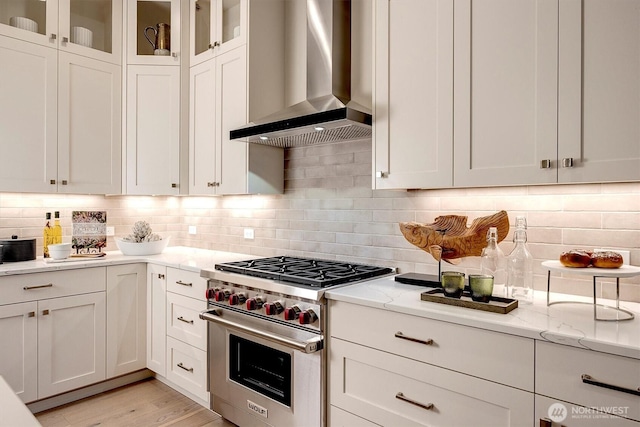 kitchen with white cabinetry, wall chimney range hood, light stone countertops, and premium stove