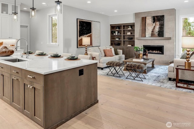 kitchen featuring light wood-style flooring, a sink, light stone counters, open floor plan, and white cabinets