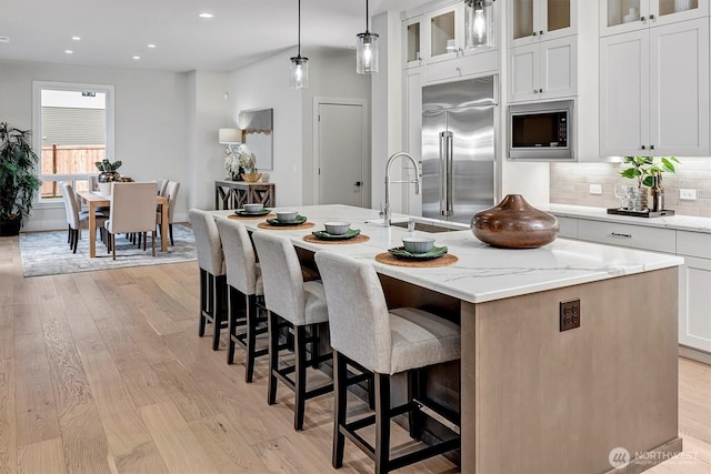 kitchen with backsplash, built in appliances, light wood-style flooring, and a center island with sink