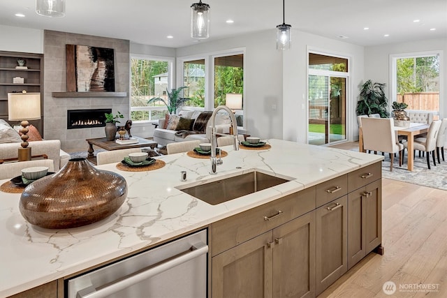 kitchen featuring light stone countertops, open floor plan, dishwasher, light wood-style flooring, and a sink