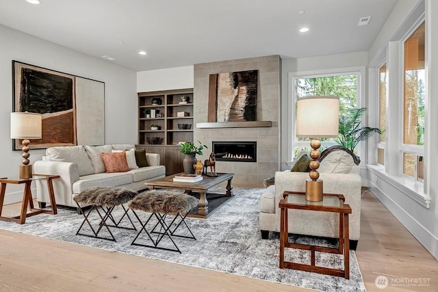 living area with a tiled fireplace, recessed lighting, wood finished floors, and visible vents