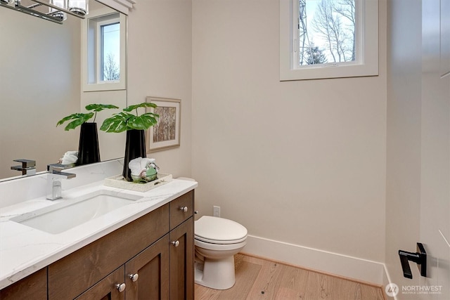 half bathroom featuring baseboards, toilet, wood finished floors, and vanity