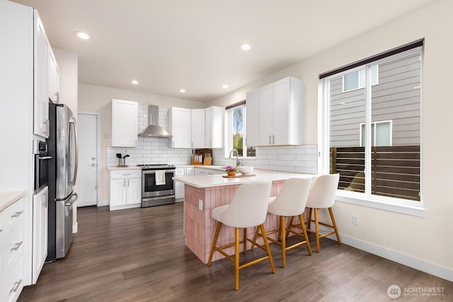 kitchen featuring wall chimney range hood, dark wood finished floors, decorative backsplash, a peninsula, and stainless steel appliances