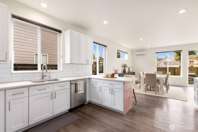 kitchen featuring dark wood-type flooring, a peninsula, stainless steel dishwasher, white cabinetry, and a sink