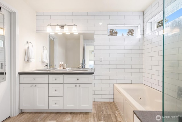 full bath featuring wood finished floors, a jetted tub, tile walls, and a sink