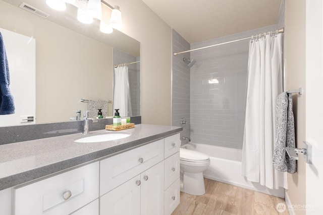 full bath with visible vents, shower / bath combo with shower curtain, toilet, wood finished floors, and vanity