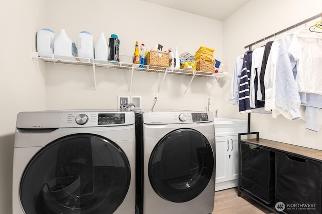 laundry area featuring washing machine and dryer, cabinet space, light wood-type flooring, and a sink