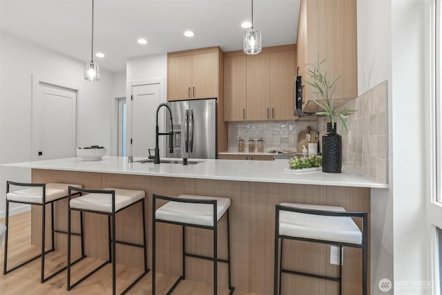 kitchen featuring stainless steel fridge with ice dispenser, a sink, decorative backsplash, light countertops, and a kitchen bar