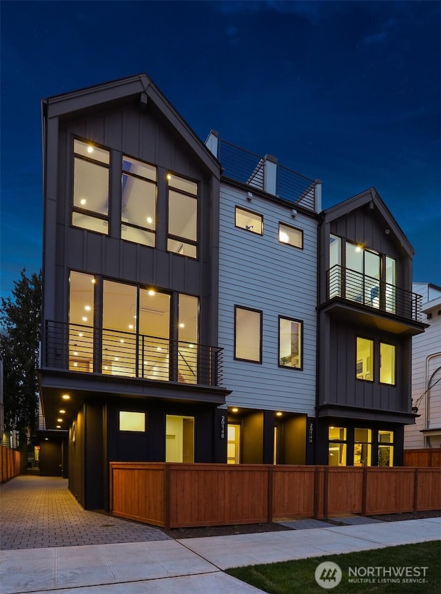 contemporary house with board and batten siding, fence, decorative driveway, a garage, and a balcony