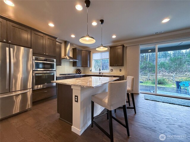 kitchen with dark wood finished floors, a center island, dark brown cabinetry, appliances with stainless steel finishes, and wall chimney exhaust hood