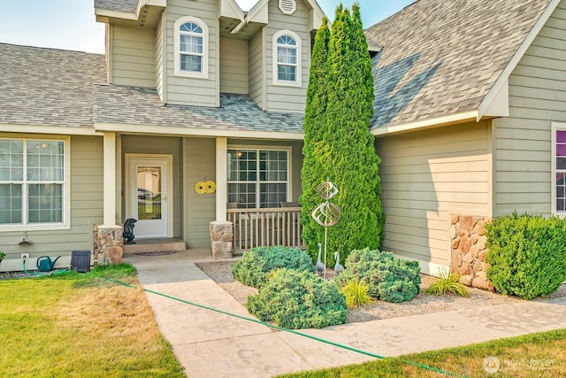 view of exterior entry featuring a porch, a yard, and roof with shingles