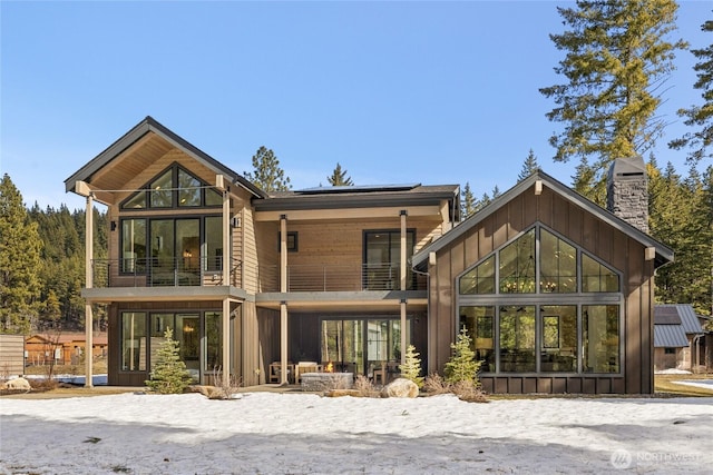 rear view of property with solar panels, a balcony, board and batten siding, and a chimney