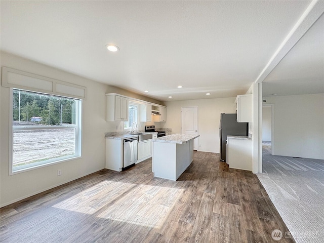 kitchen with wood finished floors, a sink, white cabinets, appliances with stainless steel finishes, and a center island