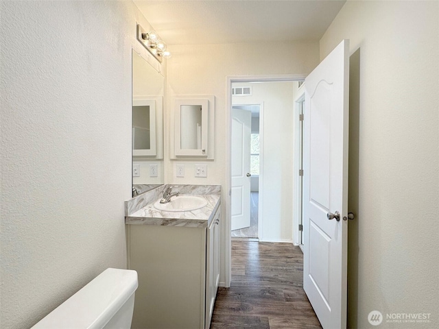 bathroom featuring visible vents, toilet, wood finished floors, a textured wall, and vanity