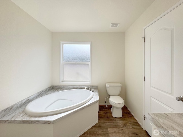 bathroom with wood finished floors, visible vents, baseboards, a garden tub, and toilet