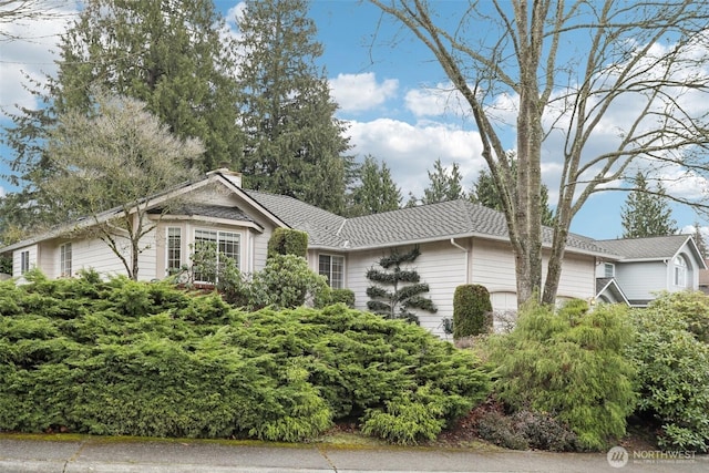 ranch-style home with a chimney, an attached garage, and a shingled roof