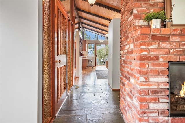 hall featuring stone tile floors, wooden ceiling, vaulted ceiling with beams, and brick wall