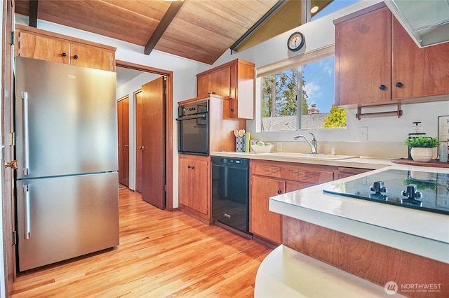 kitchen featuring vaulted ceiling with beams, light wood-type flooring, light countertops, black appliances, and a sink