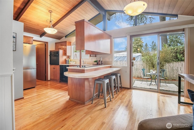 kitchen featuring black appliances, lofted ceiling with beams, light wood-style floors, a peninsula, and light countertops