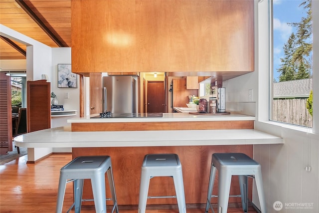 kitchen featuring black electric stovetop, beamed ceiling, wood ceiling, a peninsula, and freestanding refrigerator