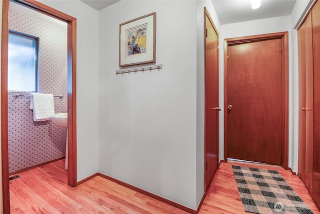 hall featuring wallpapered walls, visible vents, baseboards, and light wood finished floors