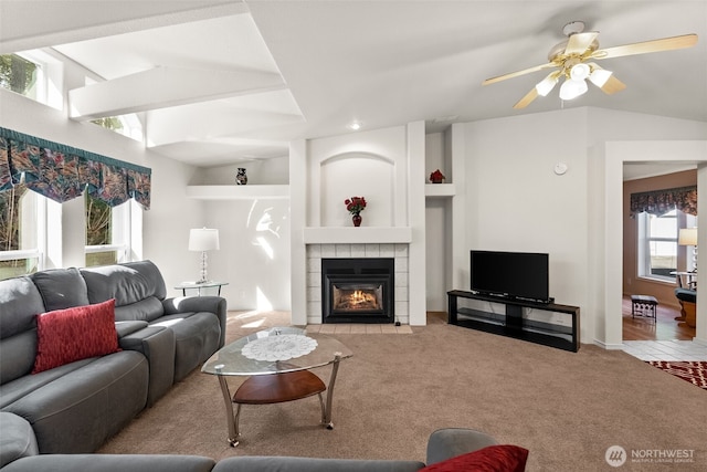 living room featuring ceiling fan, vaulted ceiling, carpet flooring, and a tile fireplace