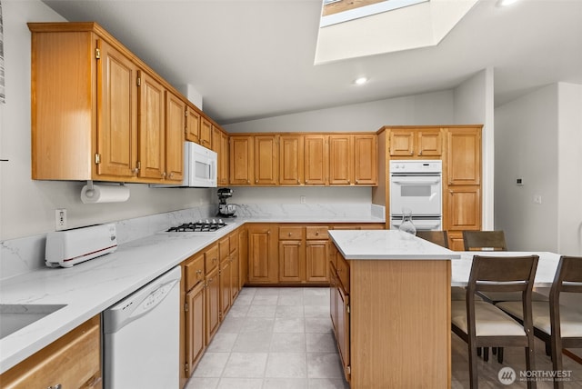 kitchen with a kitchen bar, lofted ceiling with skylight, light stone counters, a center island, and white appliances