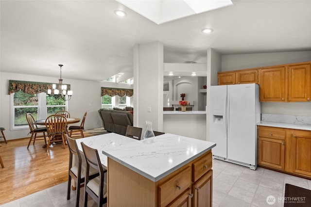 kitchen with lofted ceiling with skylight, white fridge with ice dispenser, brown cabinets, and hanging light fixtures