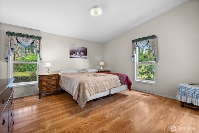 bedroom with lofted ceiling, multiple windows, baseboards, and light wood-type flooring