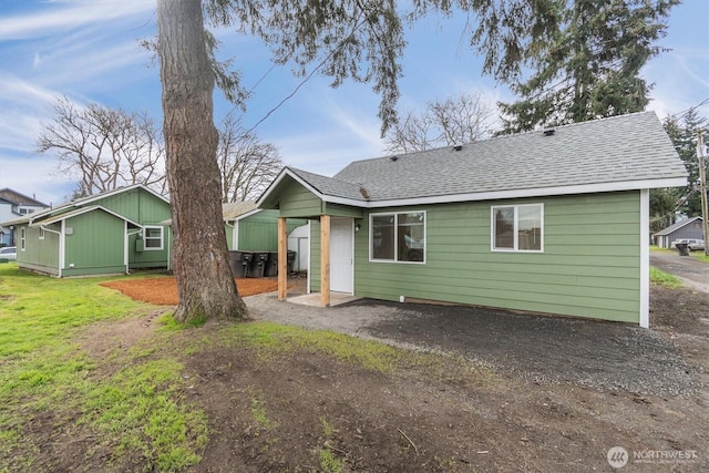 rear view of property featuring driveway, a shingled roof, and a yard