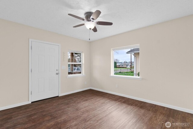 empty room with a healthy amount of sunlight, a ceiling fan, baseboards, and wood finished floors