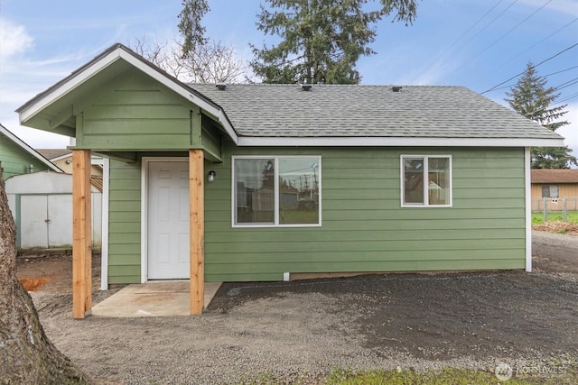 rear view of property with an outbuilding, roof with shingles, a storage shed, and fence