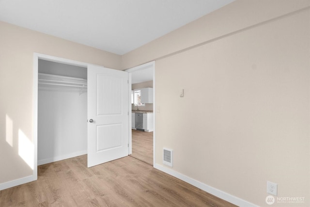 unfurnished bedroom with visible vents, baseboards, wood finished floors, a closet, and a sink