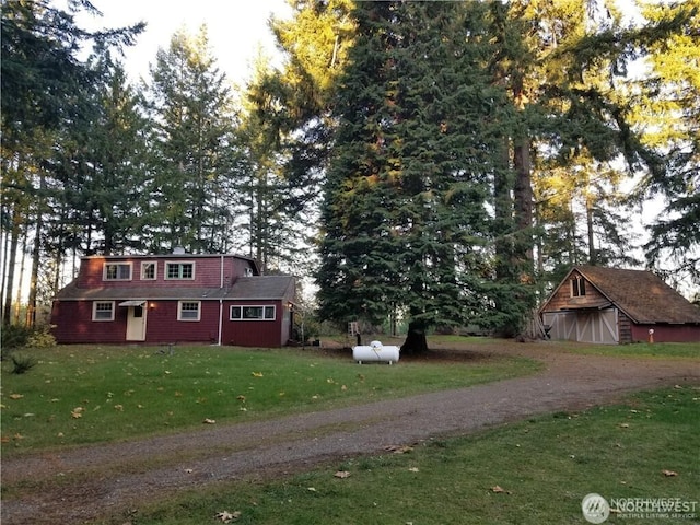 view of front of house featuring dirt driveway, an outdoor structure, and a front lawn