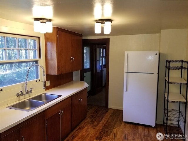 kitchen featuring a sink, backsplash, light countertops, freestanding refrigerator, and dark wood-style flooring