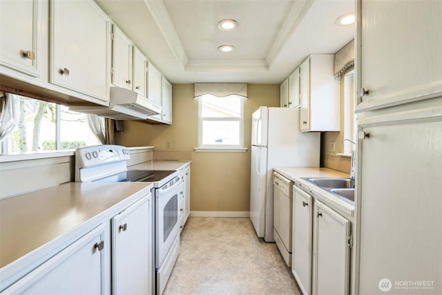 kitchen featuring under cabinet range hood, light countertops, a tray ceiling, ornamental molding, and white appliances