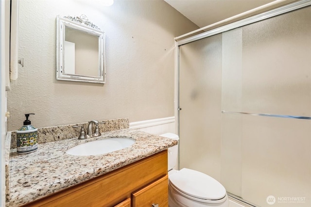 full bath featuring vanity, toilet, a stall shower, and wainscoting