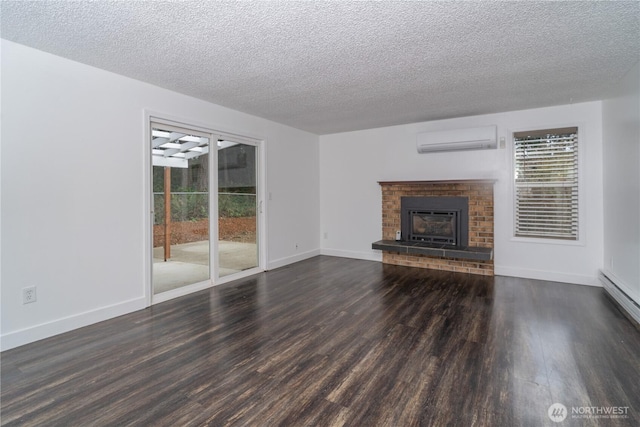 unfurnished living room with a wall mounted AC, a textured ceiling, wood finished floors, baseboards, and a brick fireplace