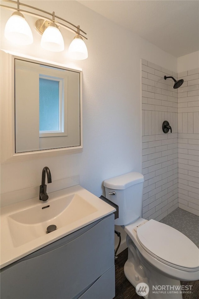 full bathroom with tiled shower, toilet, wood finished floors, and vanity