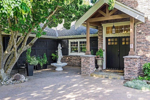 view of exterior entry featuring stone siding and a shingled roof