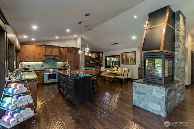 kitchen featuring high end range, dark wood-style floors, an island with sink, hanging light fixtures, and vaulted ceiling