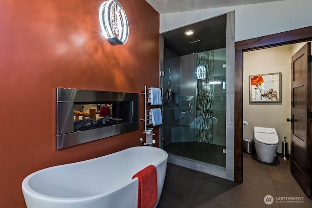 bathroom featuring a freestanding tub, toilet, a stall shower, and tile patterned flooring