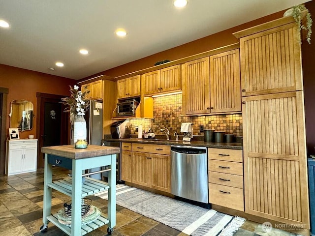 kitchen featuring dark countertops, decorative backsplash, recessed lighting, stainless steel appliances, and a sink