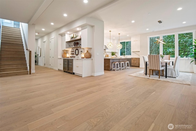 interior space featuring beverage cooler, baseboards, light wood finished floors, recessed lighting, and stairs