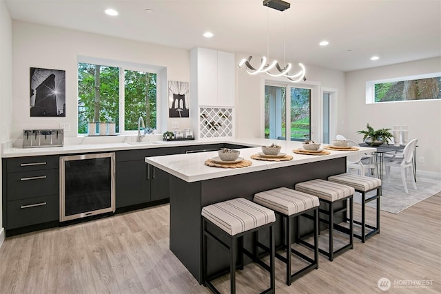 kitchen featuring light wood finished floors, beverage cooler, a breakfast bar, light countertops, and a sink