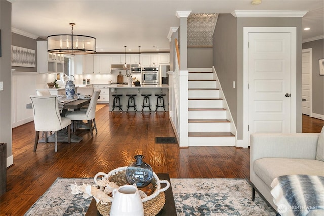 living room with stairs, visible vents, ornamental molding, and dark wood finished floors