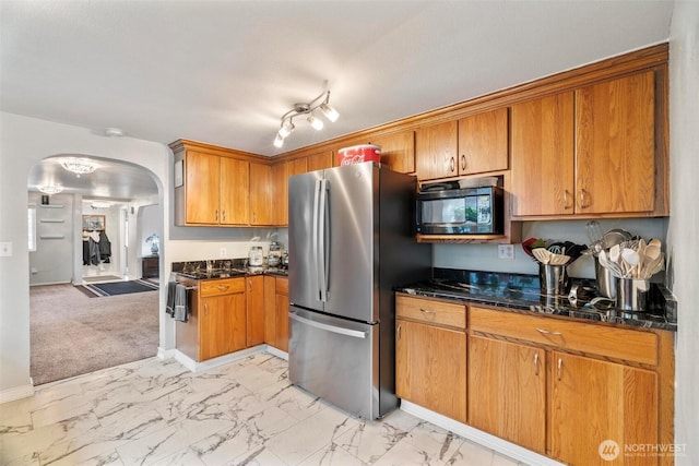 kitchen with brown cabinetry, black microwave, freestanding refrigerator, arched walkways, and marble finish floor